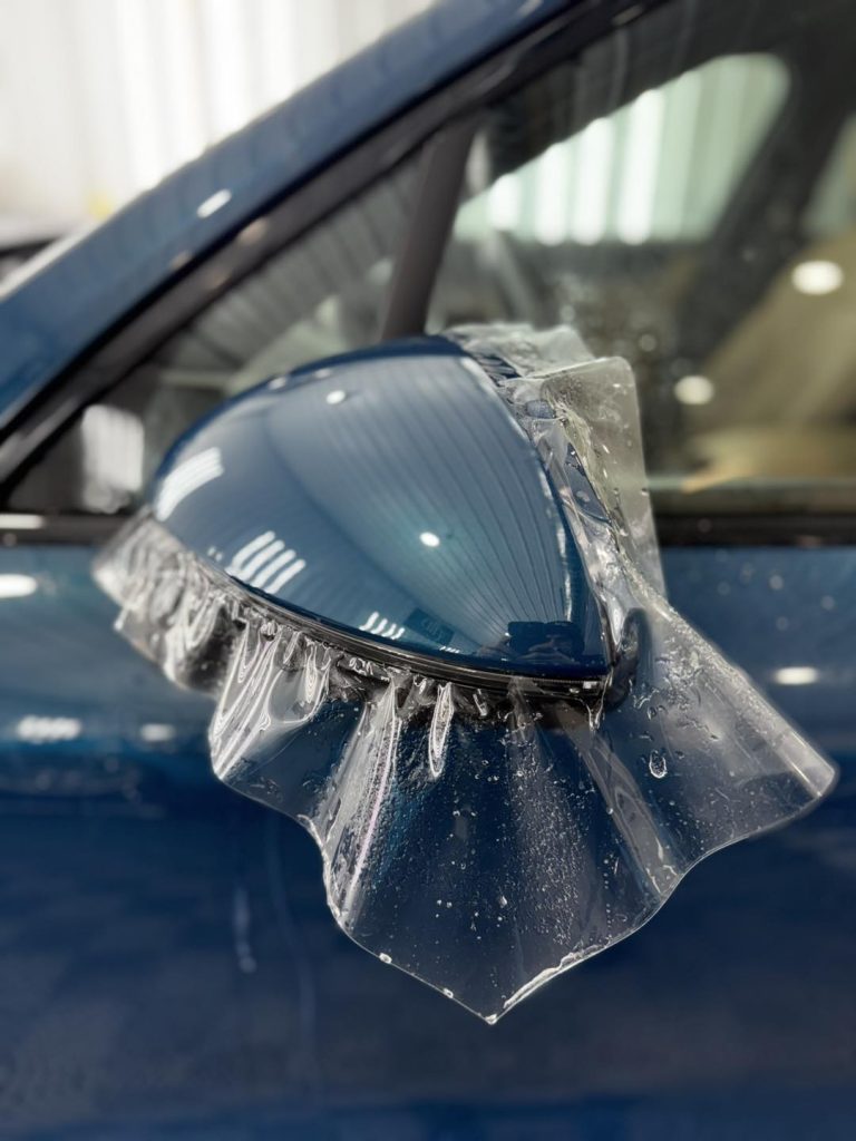 Close-up of PPF application on vehicle side mirror showing precision installation
